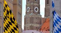 vavtrade.hu - München. München (arany-fekete) és Bajorország (fehér-kék) zászlója München belvárosában, háttérben a Frauenkirchével. Forrás: wikipedia.org